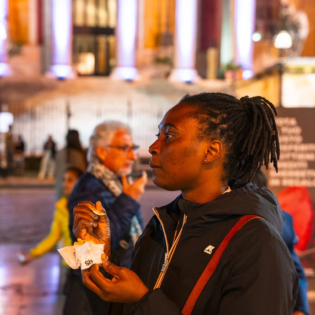 Una ragazza assaggia il gelato in piazza, di sera, davanti al Teatro Massimo illuminato